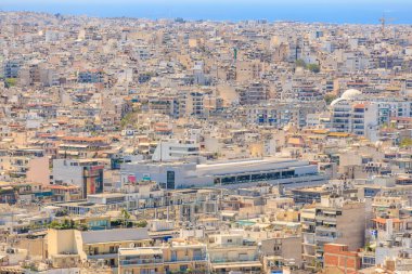 Bir sürü bina ve arka planda büyük bir su kütlesi olan bir şehir manzarası. Binaların çoğu beyaz ve etrafta çok sayıda insan var. 9 Ağustos 2024 Atina Yunanistan