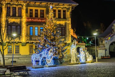 İsa 'nın doğumu sahnesi olan bir Noel ağacı bir binanın önünde parlıyor. Sahne şenlikli ve davetkar. 13 Aralık 2024 Brasov Romanya