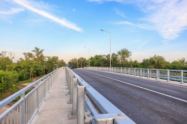 Mavi gökyüzünün altındaki ağaçların arasında metal korkulukları olan modern beton köprü. 2 Haziran 2025 Balti Moldova.