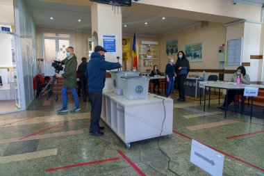 Beyaz yetişkinler kapalı sandık merkezinde seçim görevlileriyle oy veriyorlar. 21 Kasım 2021 Balti, Moldova.