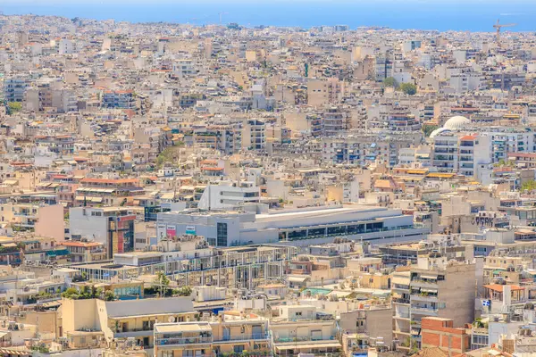 Bir sürü bina ve arka planda büyük bir su kütlesi olan bir şehir manzarası. Binaların çoğu beyaz ve etrafta çok sayıda insan var. 9 Ağustos 2024 Atina Yunanistan