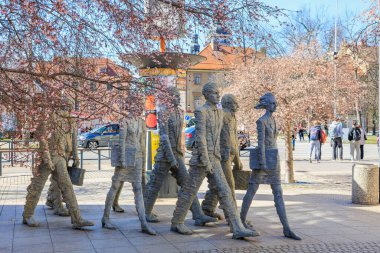 Şehir ortamında çiçek açan ağaçların arasında yürüyen insanların taş heykelleri. 21 Mart 2025, Ceske Budejovice, Çek.