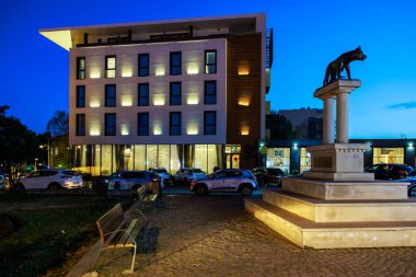 Günbatımında aydınlık pencereleri ve kurt heykeli olan modern bir bina. 3 Mayıs 2025 Romanya.