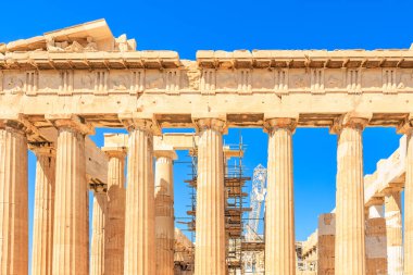 Sütunlar taştan yapılmıştır ve bir binanın parçasıdır. Bina bir şehirde ve gökyüzü mavi.