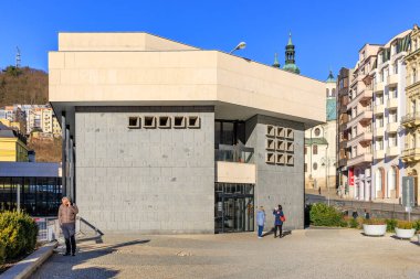 Güneşli bir günde kentsel ortamda insanların olduğu modern mimari bina. 18 Mart 2025, Karlovy Vary, Çek Cumhuriyeti.