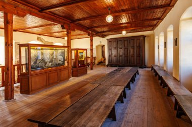 Historic monastery refectory with wooden furniture and art display. March 18, 2025, Loket, Czech Republic.