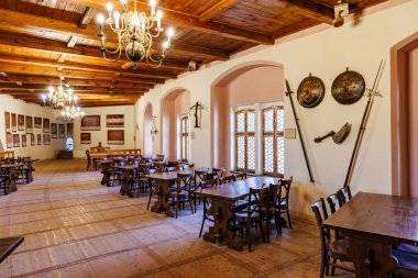 Rustic medieval dining hall with wooden furniture and antique chandeliers. March 18, 2025, Loket, Czech Republic.