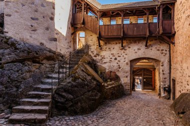 Medieval stone castle courtyard with wooden balcony and cobbled pathway. March 18, 2025, Loket, Czech Republic.