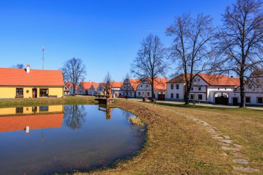 Picturesque village with reflective pond and red-tiled roofs on a clear day. March 21, 2025, Holasovice, Czechia.