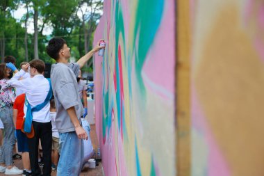 Young asian male creating colorful street art mural in public park. May 31, 2024 Balti Moldova.