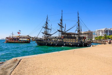 A large black ship is docked at the beach. The ship is surrounded by a group of people. August 8, 2024 Thessaloniki Greece