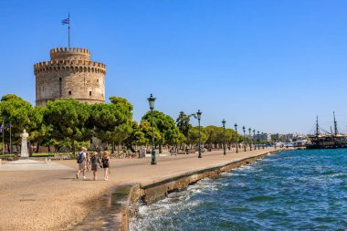 Bir grup insan büyük bir kule yakınında bir sahil boyunca yürür. Gökyüzü açık ve su sakin. 8 Ağustos 2024 Selanik Yunanistan