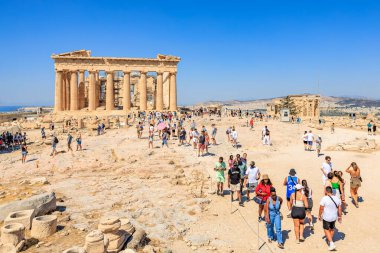 Büyük bir grup insan büyük bir binanın etrafında toplanıyor, muhtemelen bir tapınak ya da anıt. Gökyüzü açık ve mavidir, ve güneş parlıyor. 9 Ağustos 2024 Atina Yunanistan