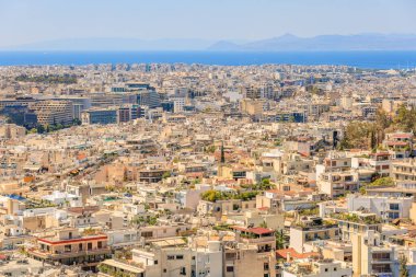 Arka planda büyük bir su kütlesi olan bir şehir manzarası. Şehir yüksek binalarla dolu ve bir sürü yeşil alanı var. 9 Ağustos 2024 Atina Yunanistan