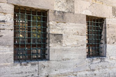 Historic stone building with iron barred windows reflecting sunlight.