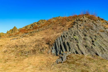 Dramatic basalt columns amidst autumn landscape under clear blue sky.