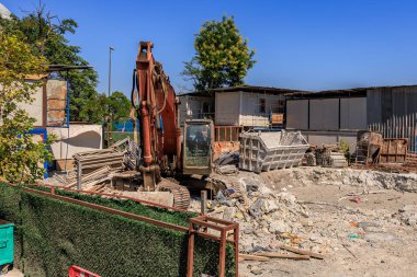 Excavator at construction site with rubble and containers in urban setting. August 12, 2025 Istanbul Turkey.