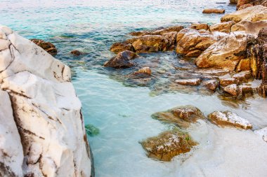 Önünde bir su kütlesi olan kayalık bir sahil. Su berrak ve sakin.