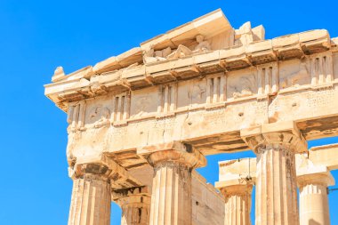 Bina, arka planında mavi gökyüzü olan bir tapınak. Bina taştan yapılmış ve bir sürü sütunları var.