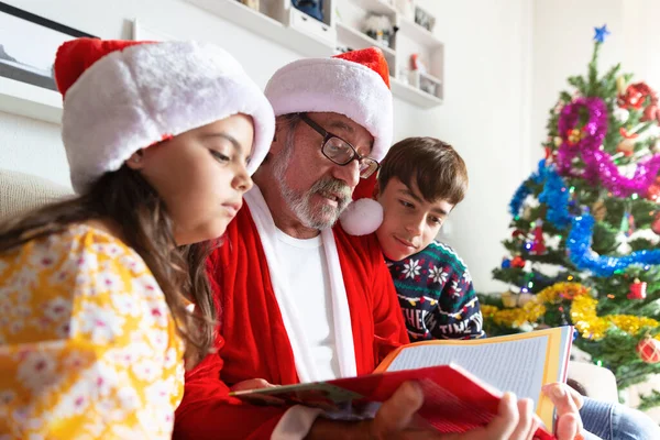 Noel Baba Kılığındaki Yaşlı Adamın Evde Iki Çocuğa Masal Okuduğu — Stok fotoğraf