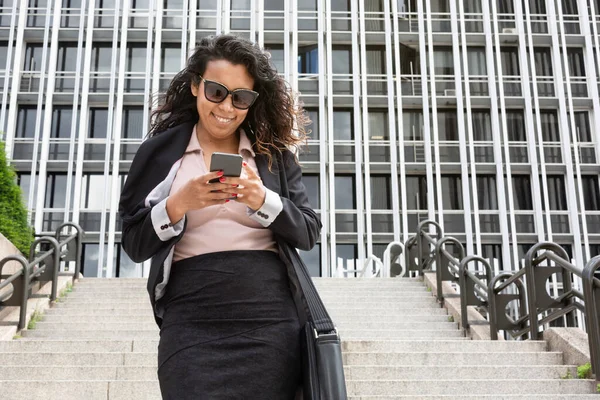 Smiling young latina business woman using her mobile phone outdoors. Space for text.