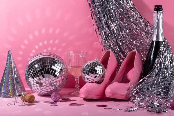 Glass of champagne with silver mirror disco ball on pink background. New year party composition
