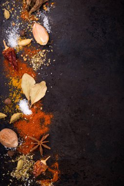 Different spices and herbs on a black background. Paprika, curry, nutmeg, cinnamon, bay leaf, salt, pepper, cardamom. Space for text
