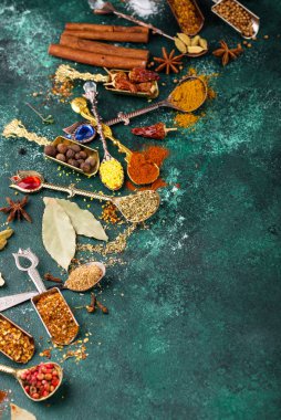 Assortment of diffferent Indian spices and herbs on spoon on green background