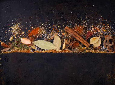 Different spices and herbs on a black background. Paprika, curry, nutmeg, cinnamon, bay leaf, salt, pepper, cardamom. Space for text