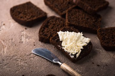 Kahverengi arka planda tereyağlı koyu bir ekmek dilimliyor.