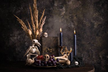 Halloween still life with skull, bones, candles and black cake. Dark table setting