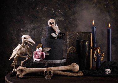 Halloween still life with skull, bones, candles and black cake. Dark table setting
