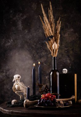 Halloween still life with skull, bones, candles and black cake. Dark table setting