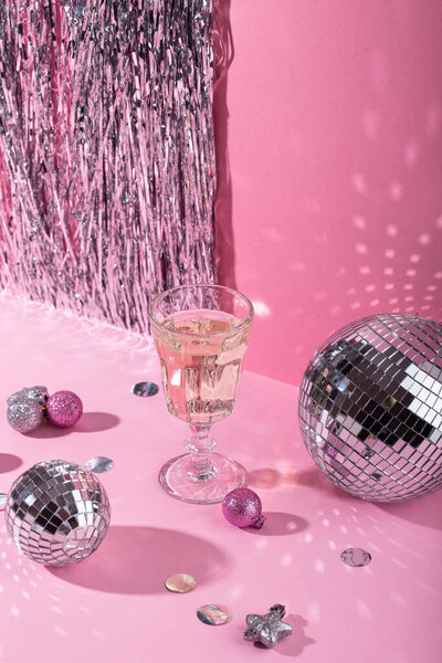 Бокал шампанского с серебряным зеркальным диско шаром на розовом фоне. Новогодний состав партии