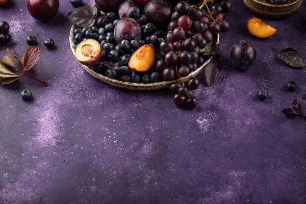 Assortment of purple fruit plum, grape, blueberry and basil on violet background