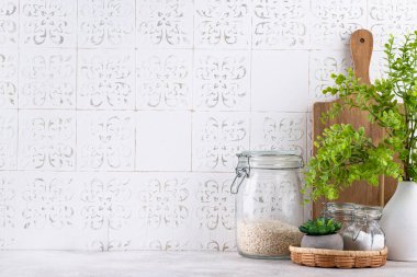 Mutfak tezgahının üstünde kavanozlar ve beyaz arka planda kesim tahtaları var.