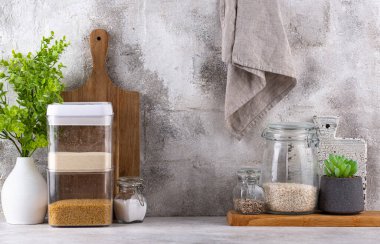 Mutfak tezgahının üstünde kavanozlar ve beyaz arka planda kesim tahtaları var.