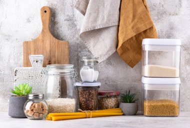 Mutfak tezgahının üstünde kavanozlar ve beyaz arka planda kesim tahtaları var.