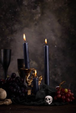 Halloween still life with skull, bones, candles and black cake. Dark table setting