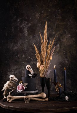 Halloween still life with skull, bones, candles and black cake. Dark table setting