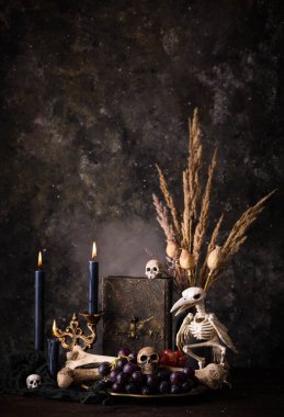 Halloween still life with skull, bones, candles and black cake. Dark table setting