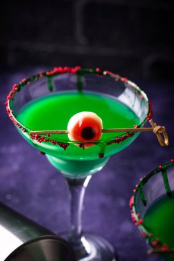 Canlı yeşil cadılar bayramı kokteyli, martini bardağında kırmızı göz süslemesi.