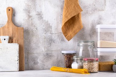 Mutfak tezgahının üstünde kavanozlar ve beyaz arka planda kesim tahtaları var.