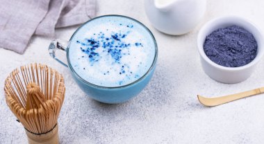 Ahşap çırpmalı mavi kibrit latte içeceği ve mermer zemin üzerinde küçük bir kase kibrit tozu..