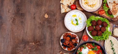 Humus, pide ekmeği, sahanda yumurta ve taze sebzeler de dahil olmak üzere ahşap bir masada geleneksel Orta Doğu kahvaltı yemekleri..