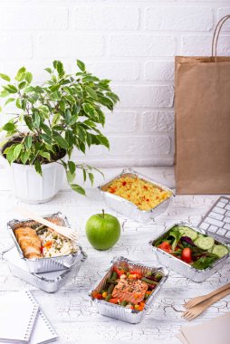 Besleyici ve lezzetli ev yapımı yemekler servis konteynırlarında saksı bitkisi olan beyaz bir masada..