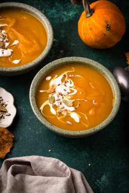 Yeşil zemin üzerinde iki kase kremalı balkabağı çorbası, kızarmış fındıkla süslenmiş..