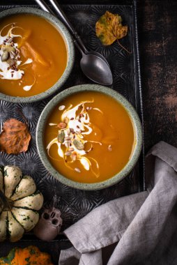 İki kase ılık, portakallı balkabağı çorbası ve sonbahar yaprakları..