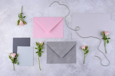 Pembe bir zarf, gri zarflar ve açık gri arka planda pembe gül tomurcukları içeren romantik bir kompozisyon..