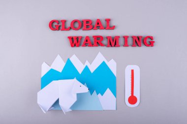 Resim, mavi kağıt dağları ve kırmızı Küresel Isınma metnine karşı bir kutup ayısının kağıt kesimini betimliyor..